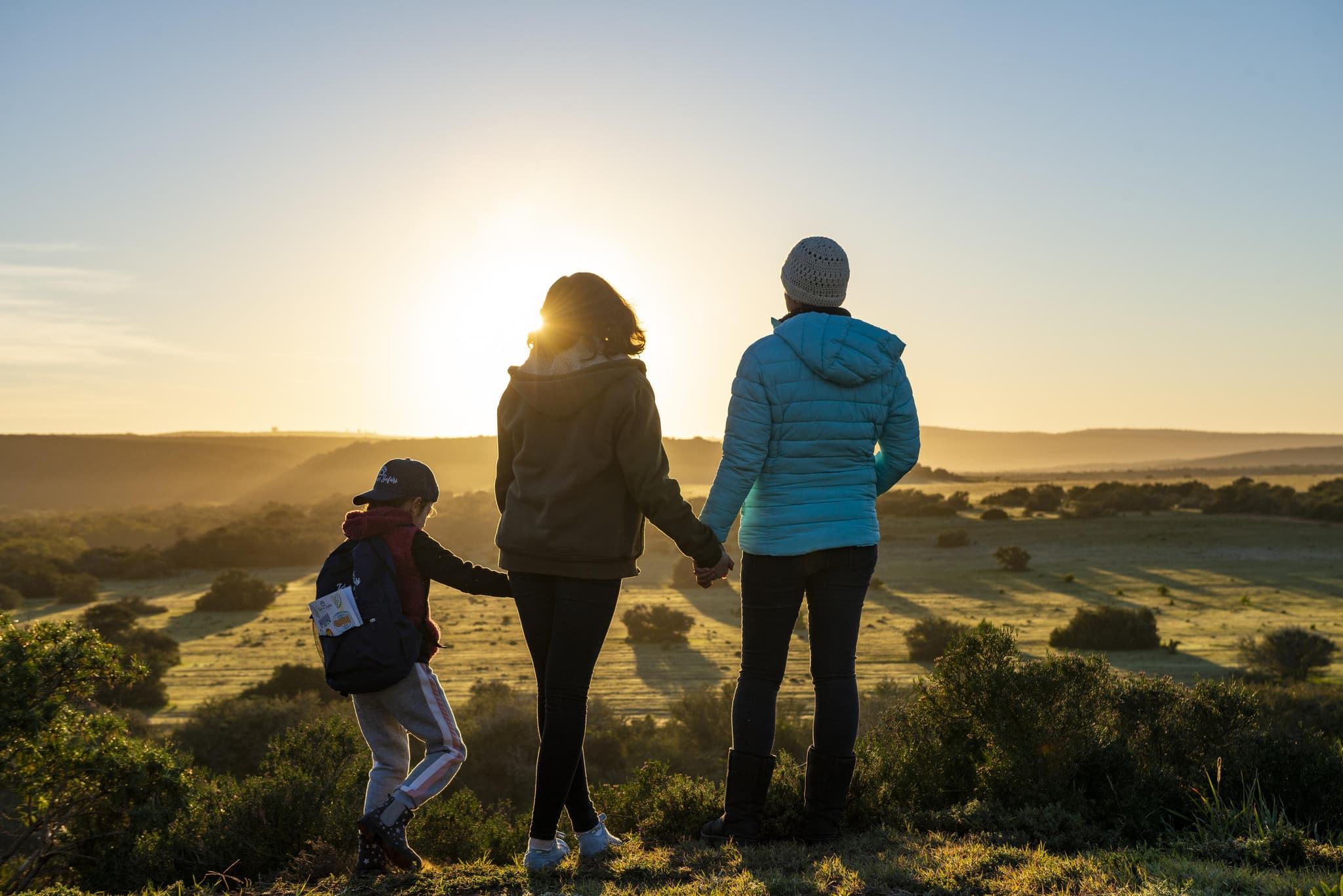 Family holding hands watching a golden sunrise over rolling green hills